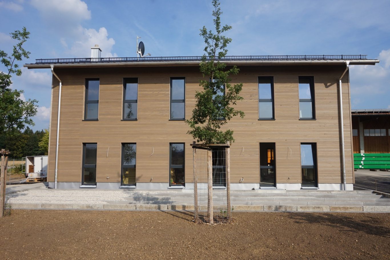 Zweiäugiges, modernes Gebäude mit Holzfassade und Solarpanelen auf dem Dach.